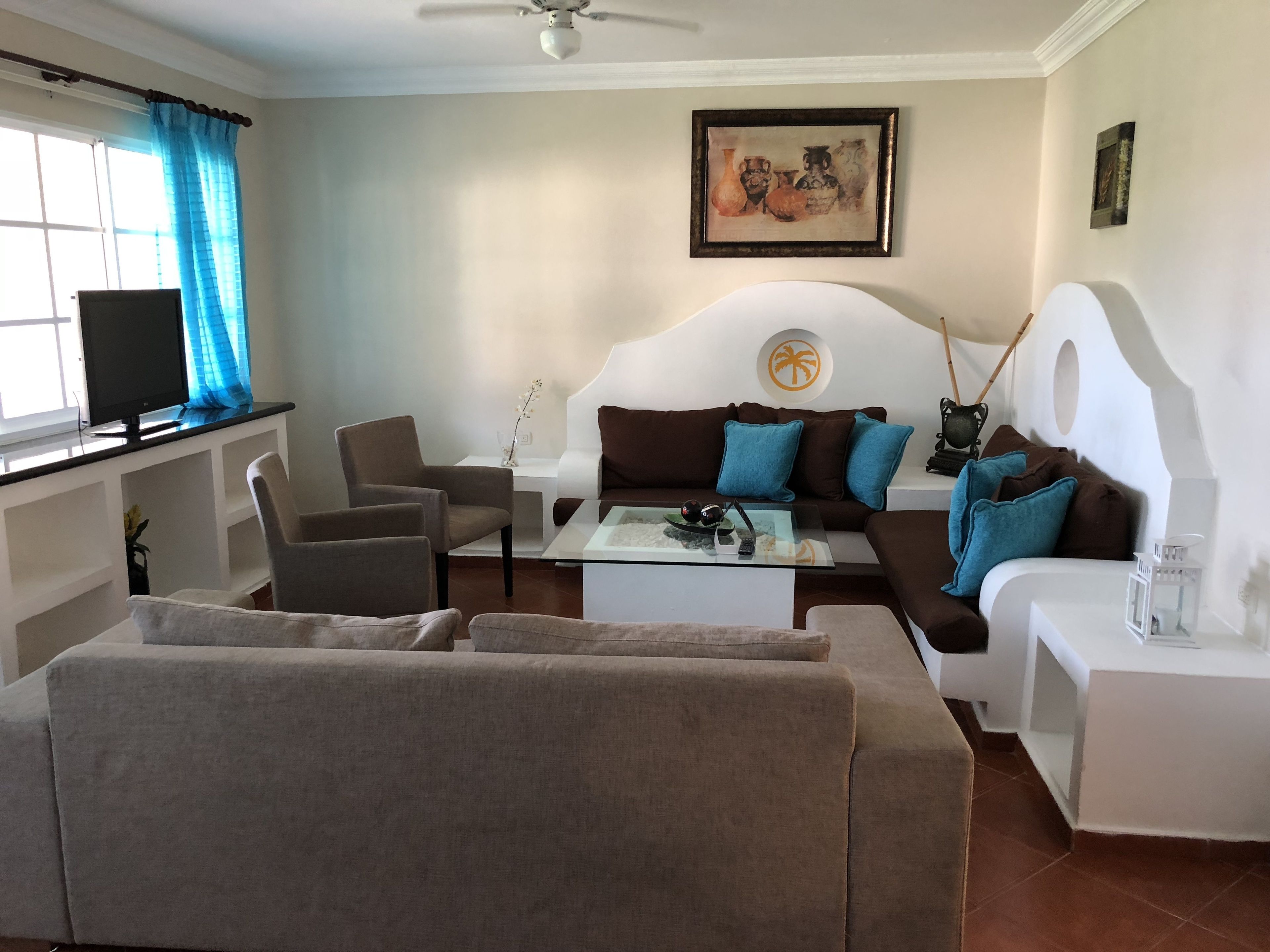 A living room with a white sofa, brown armchairs, a coffee table, and a television on a stand.