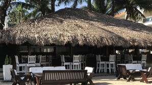 A beachside lounge with thatched umbrellas, white and wooden lounge chairs, and a sandy floor. - Lifestyle Kosher Crown Villas (Puerto Plata)