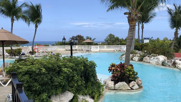 A pool area with lounge chairs, palm trees, and a view of the ocean. - Lifestyle Kosher Crown Villas (Puerto Plata)