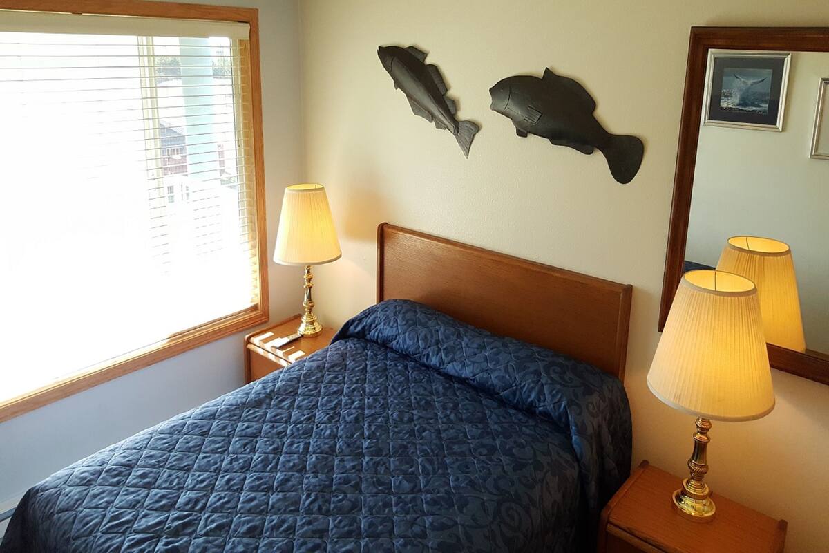A hotel room with a bed, two wall-mounted fish decorations, a window with blinds, and two bedside lamps.