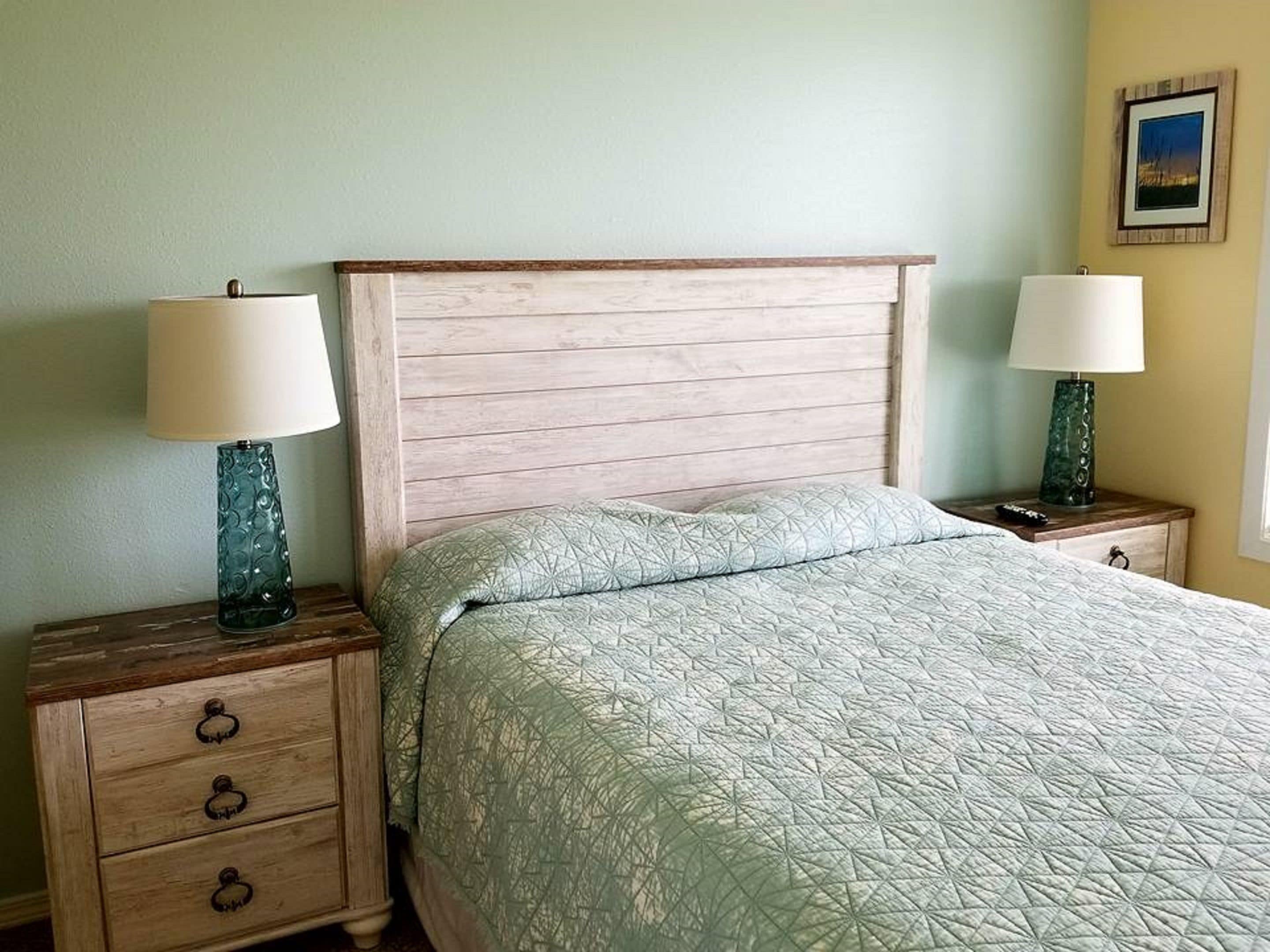 A bedroom with a wooden headboard, two bedside tables with lamps, a bed with a quilted bedspread, and a nightstand with drawers.