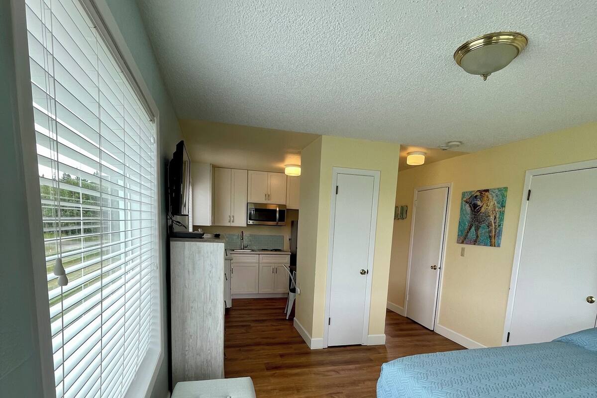 A compact bedroom with a single bed, a bench, and a view through a window with blinds.