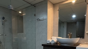 A modern bathroom with a glass-enclosed shower, a large sink with a vessel basin, and a dark-toned vanity with cabinets. - Hotel de Papae Intl (Islamabad)