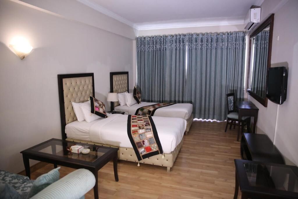 A hotel room with two beds, a television, a desk, and a chair.
