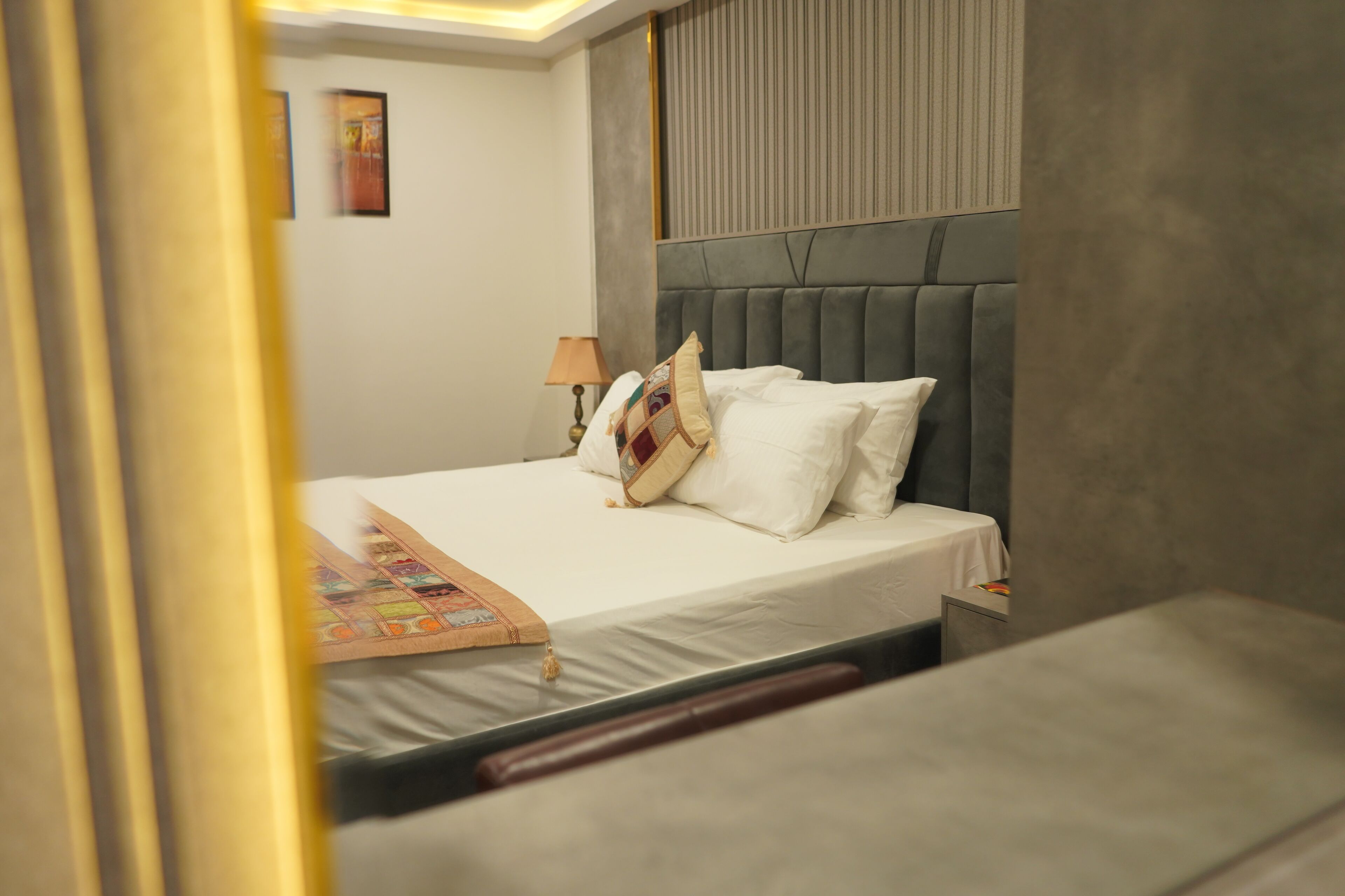Un letto rifatto con lenzuola bianche e cuscini decorativi, una lampada da comodino e un quadro appeso al muro.