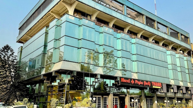 A multi-story building with a modern glass facade, a sign for 'Hotel de Papaye Restaurant', and a flagpole. - Hotel de Papae Intl (Islamabad)