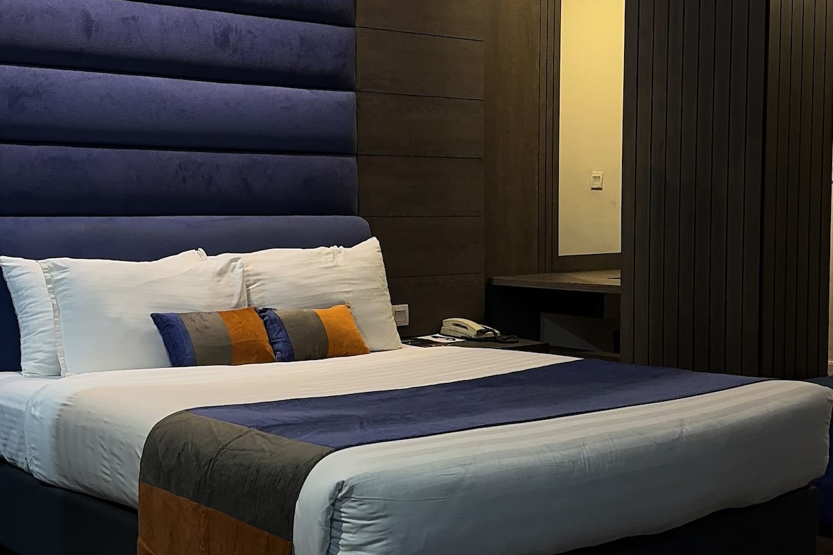 A modern hotel room with a large bed, a bedside table, a nightstand, a glass coffee table, a tissue box, and a ashtray.