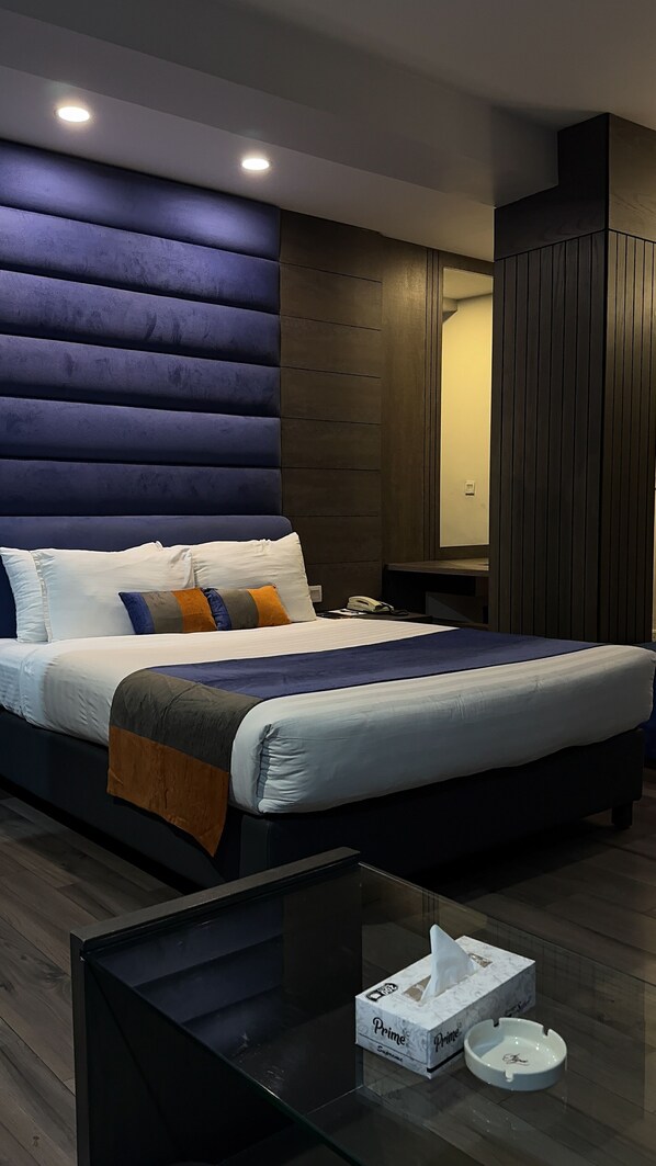 Een moderne hotelkamer met een groot bed, een nachtkastje, een glazen salontafel, een zakdoekendoos en een asbak.