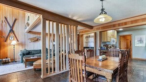 Un vaste espace de vie comprenant une table à manger en bois, des chaises et un canapé. On aperçoit une cuisine à l’arrière-plan, avec des meubles de rangement en bois et un four à micro-ondes.