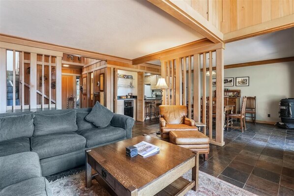 A spacious living room with a grey sofa, a wooden coffee table, and a leather armchair. A staircase leads to an upper level. - 31 Night- Pet-Friendly Bluff Unit: Panoramic Lake Views & Trailside Living (Tahoe City)
