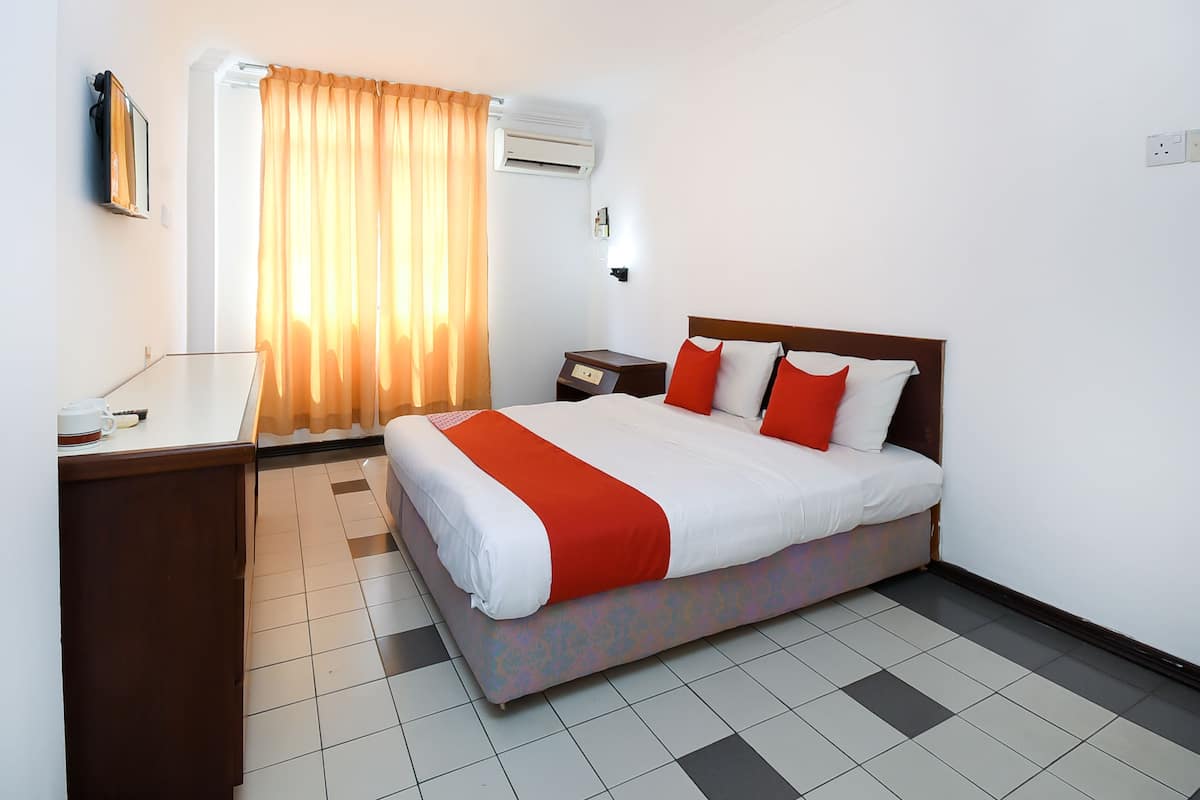 Une chambre d’hôtel comprenant un lit, un bureau, une chaise, une table de chevet, un climatiseur et une fenêtre avec des rideaux.