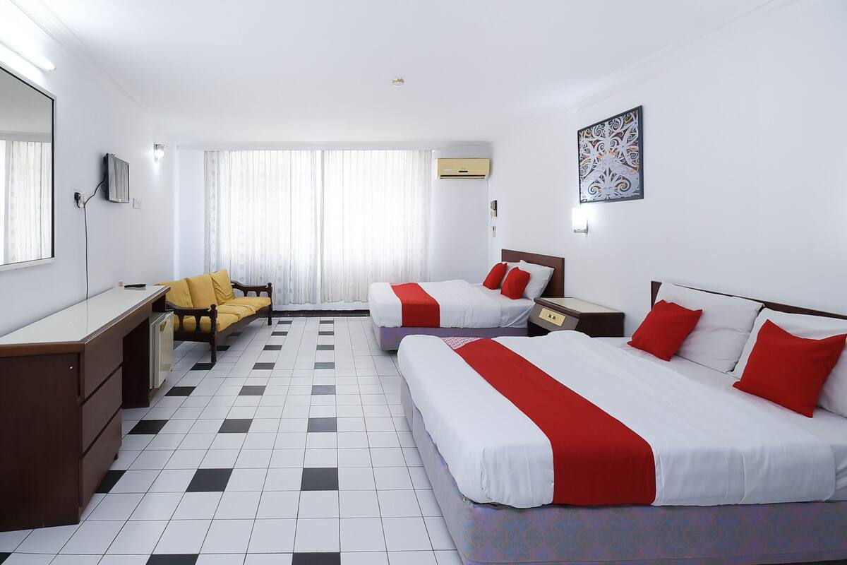 Une chambre d’hôtel avec deux lits, un bureau, une chaise et une grande fenêtre avec des rideaux.
