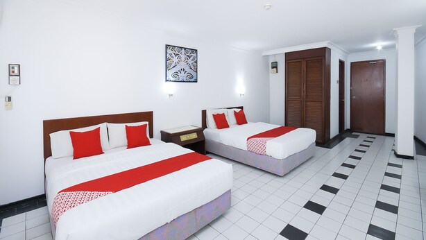 A hotel room with two beds, white walls, a patterned floor, and a wooden door.