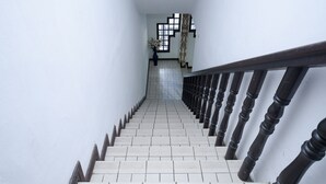 A staircase with white tiles and dark balusters, leading to a room with a patterned wall and a vase of flowers.