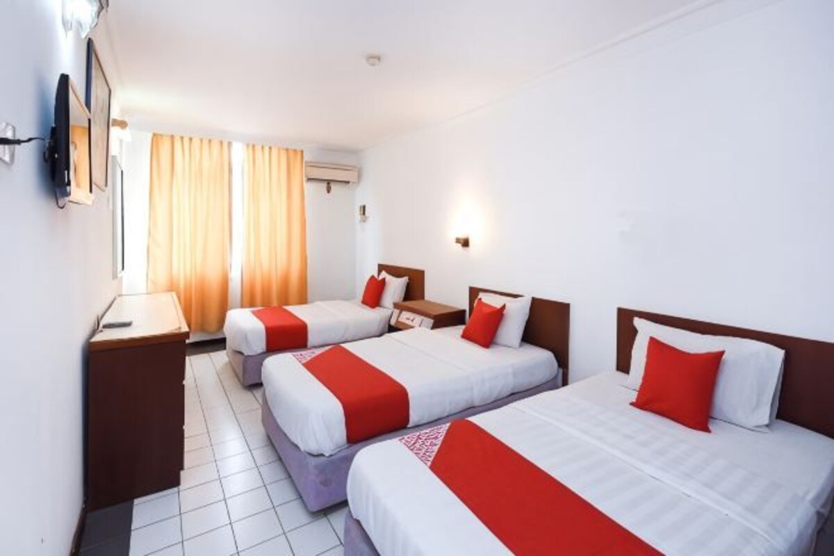 A hotel room with three beds, a TV, a desk, and a window with curtains.