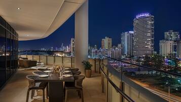 A rooftop terrace with a dining table set for four, overlooking a city skyline at night.