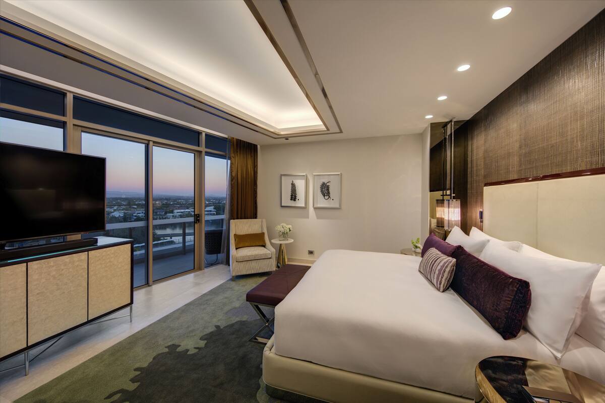 A modern hotel room with a large bed, a flat-screen TV, a seating area, and a city view.