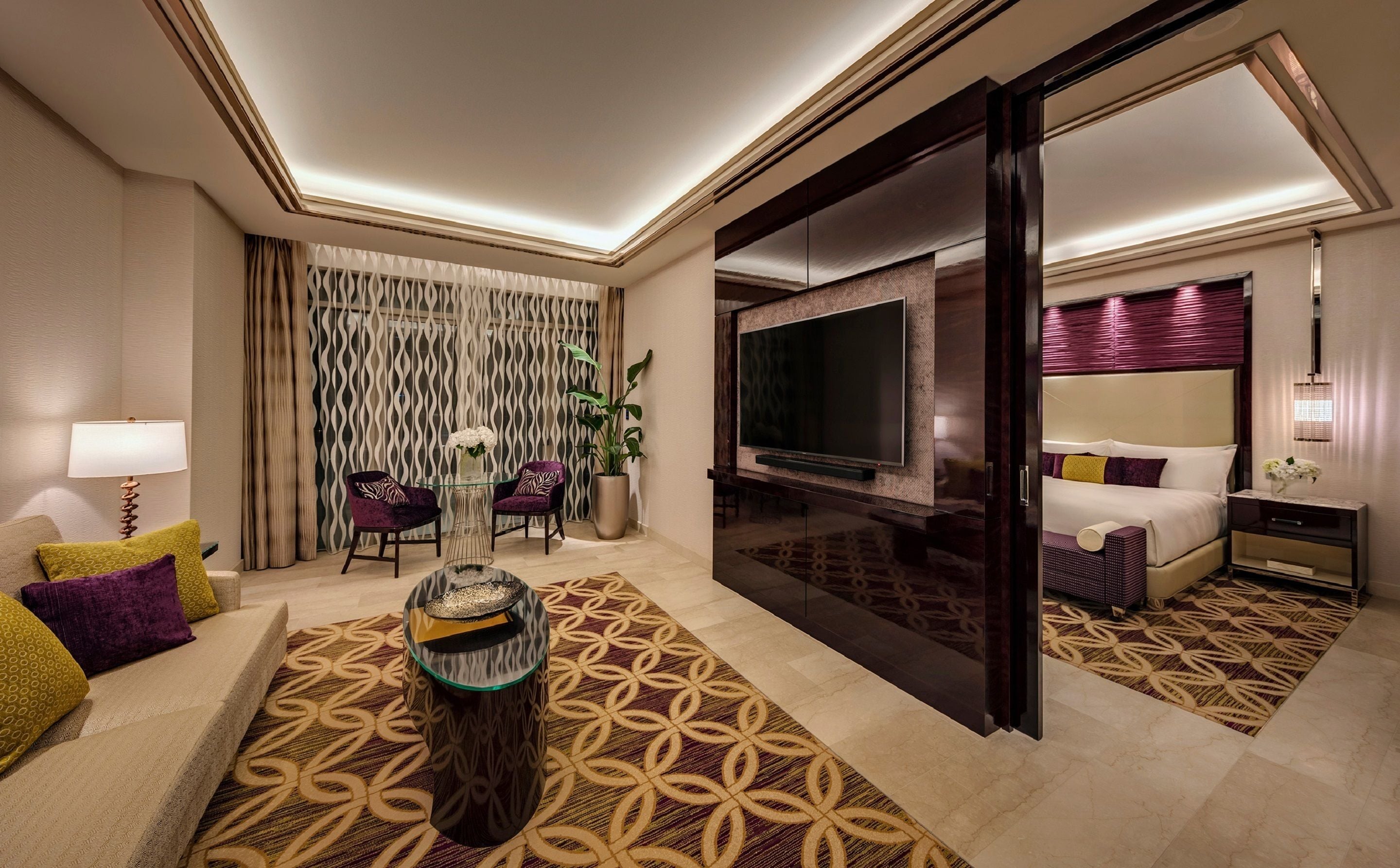 A hotel room with a sofa, a coffee table, a TV, a bed, and a sliding door.