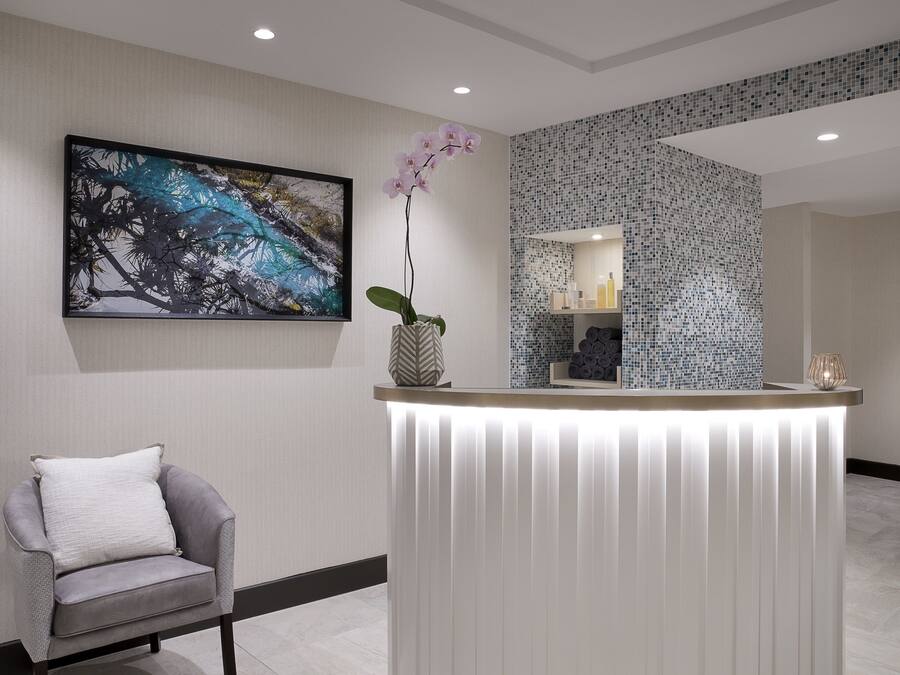 A reception area with a modern reception desk, a chair, a large abstract painting, and a decorative orchid.