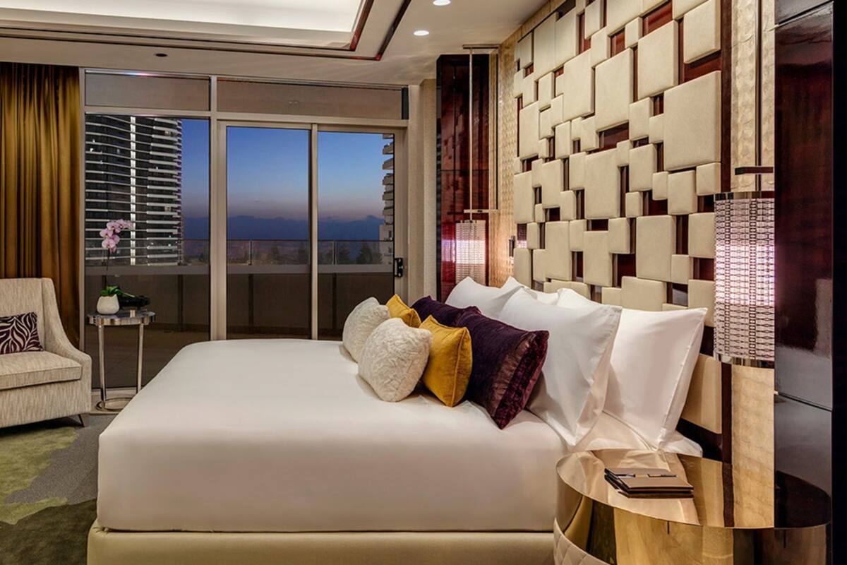 A modern hotel room with a large bed, a TV, a chair, and a balcony with a view.