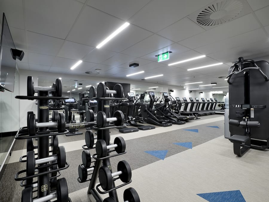 A gym with various exercise equipment, including treadmills and weight machines, arranged in rows.