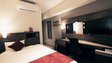 A hotel room with a bed, a desk, a chair, a TV, and an air conditioning unit.