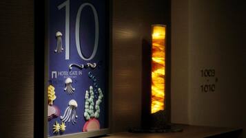 A framed number '10' with a hotel name and decorative elements, a tall pillar with a warm light, and a wall with room numbers '1003' and '1010'.
