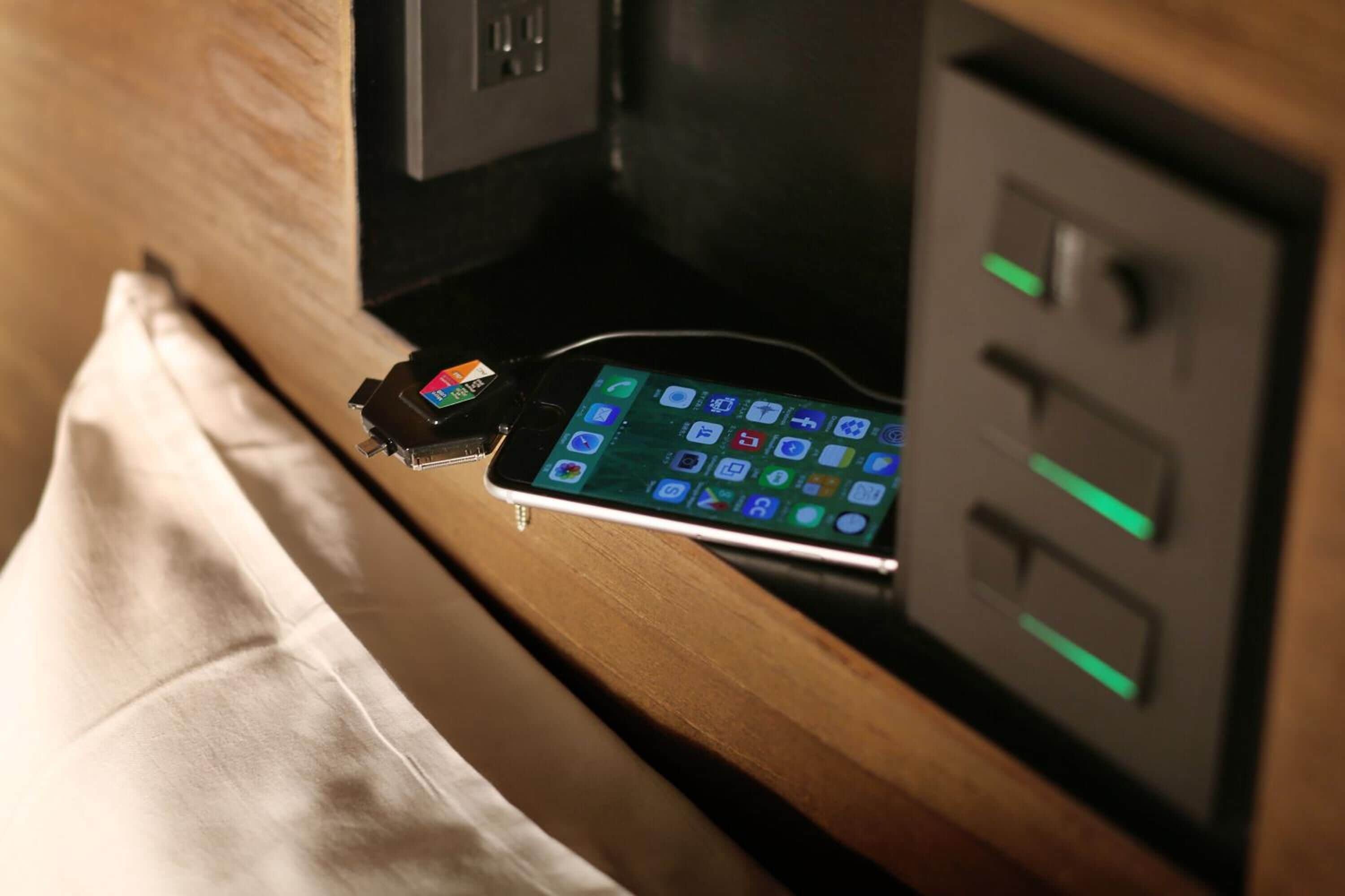 A smartphone charging on a wooden surface with a power outlet and a control panel nearby.