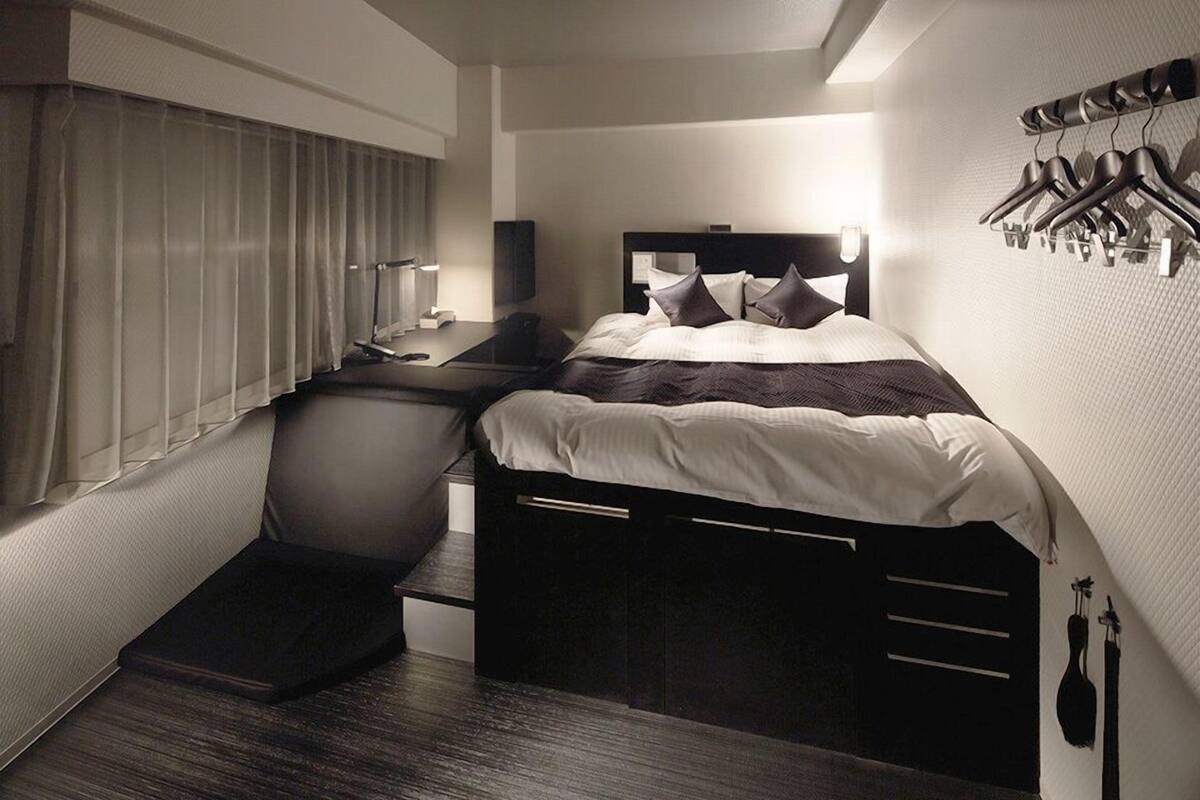 Quarto de hotel moderno com uma cama, mesa de cabeceira e escrivaninha com cadeira.