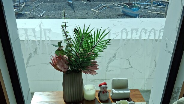 Un balcón con una mesa dispuesta para el desayuno, una planta en maceta y vistas a barcos en el agua.