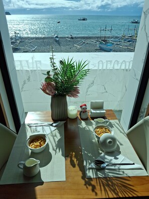 A balcony with a table set for breakfast, a potted plant, and a view of boats on the water. - Cave beach Resort Boutique Accomodation (Dingalan)