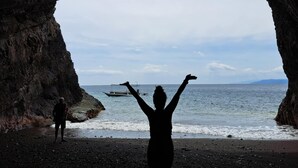 Una persona de pie en una estructura parecida a una cueva, con vista al mar y un barco a la distancia.