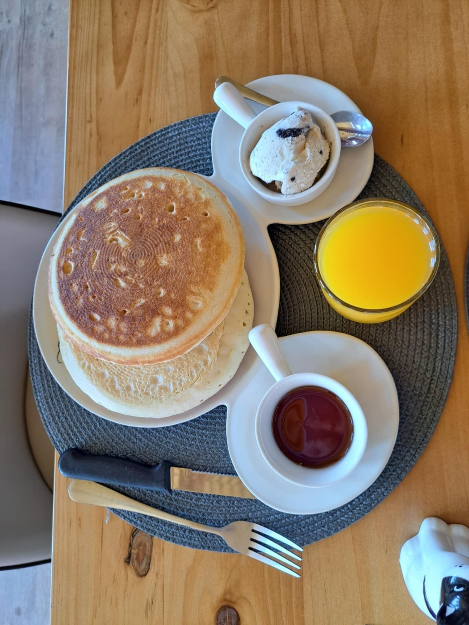 Prato de café da manhã com panquecas, uma xícara de café, um copo de suco de laranja e um potinho de geleia.