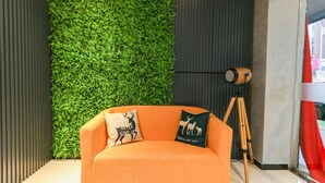 A modern interior with a green vertical garden, an orange sofa with decorative pillows, and a wooden tripod.