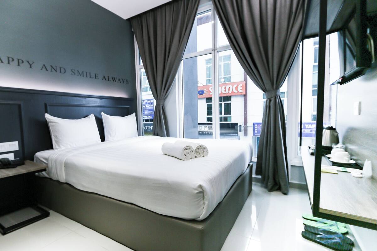 A hotel room with a neatly made bed, a bedside table with a phone, and a view of the street outside.