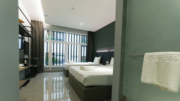 A modern hotel room with a large bed, a smaller bed, a desk with a chair, and a large window.