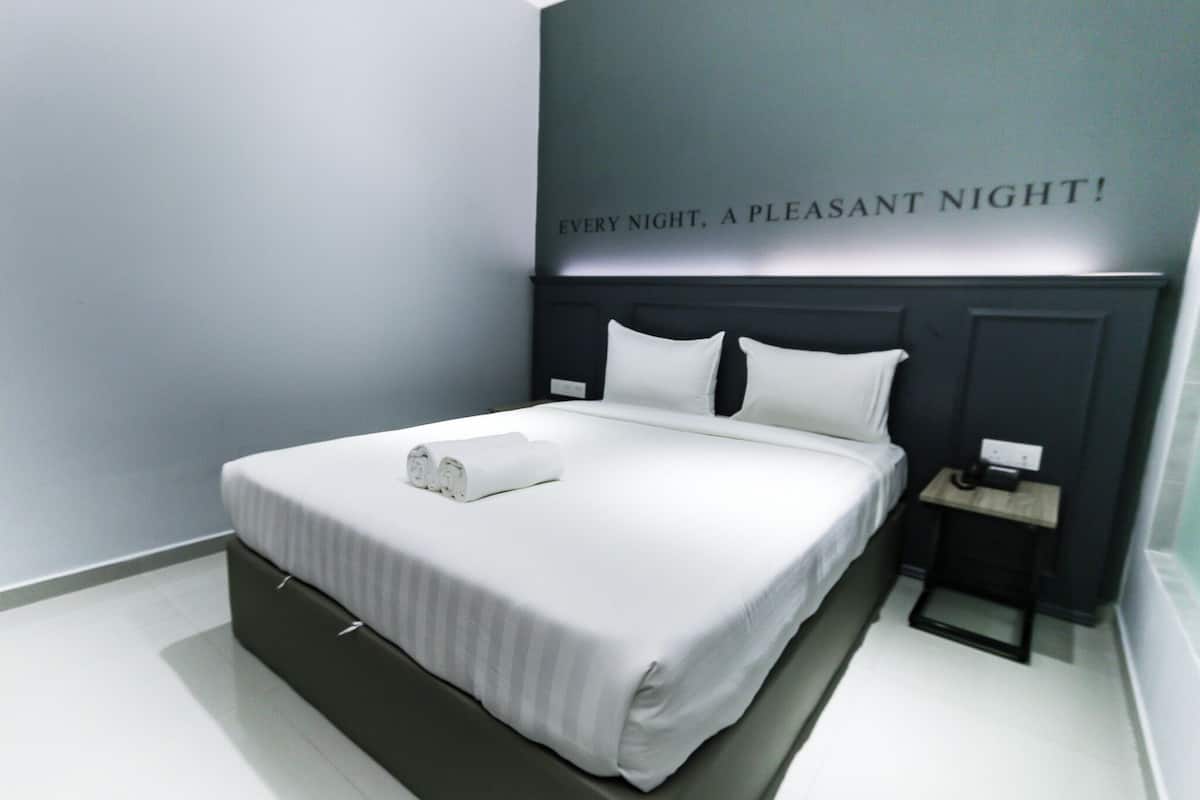 A neatly made bed with white linens and a rolled towel, a bedside table with a lamp, and a wall with a motivational quote.