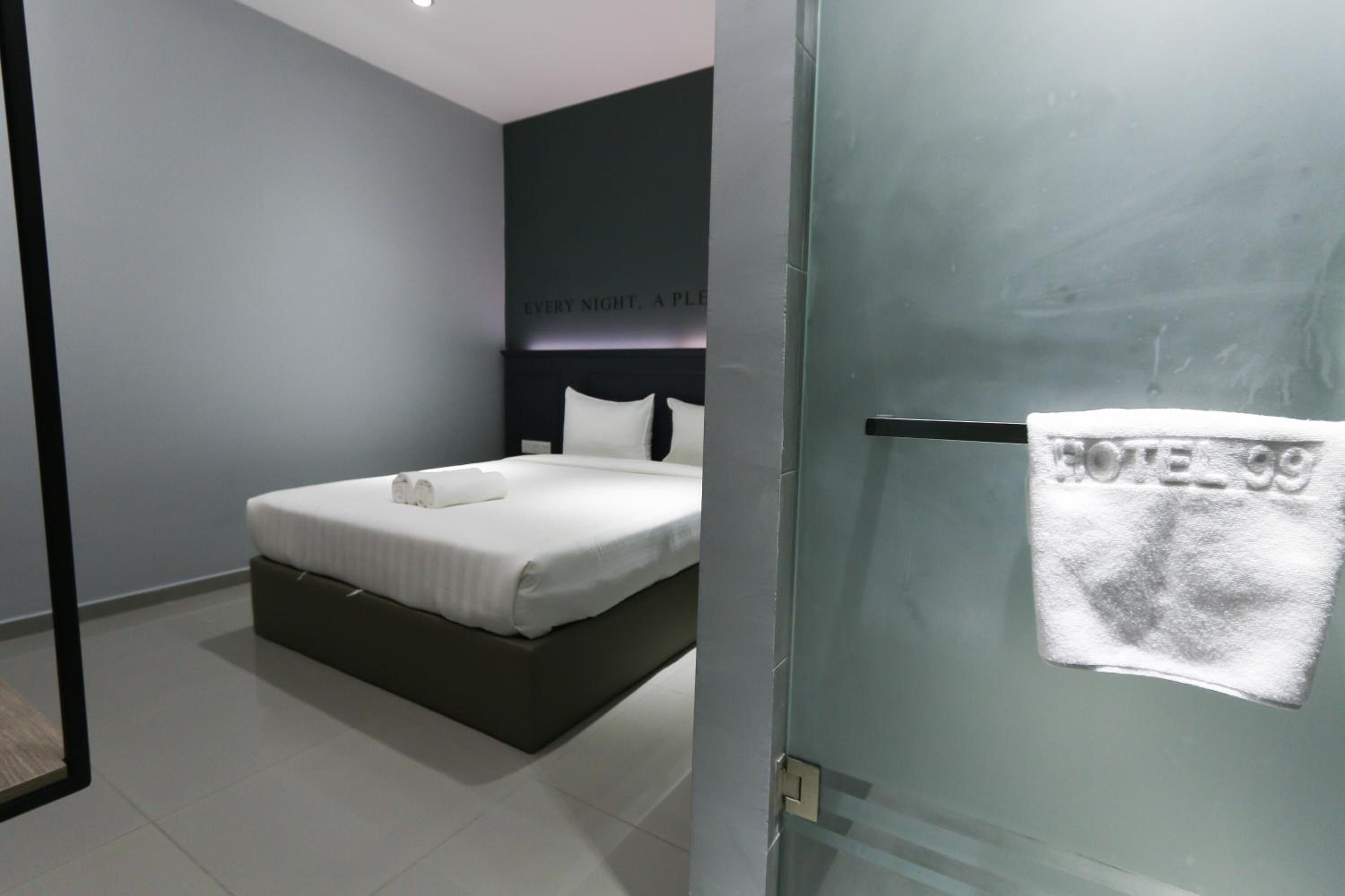 Une chambre d’hôtel moderne avec un lit, une tête de lit sombre et une serviette accrochée à la porte.