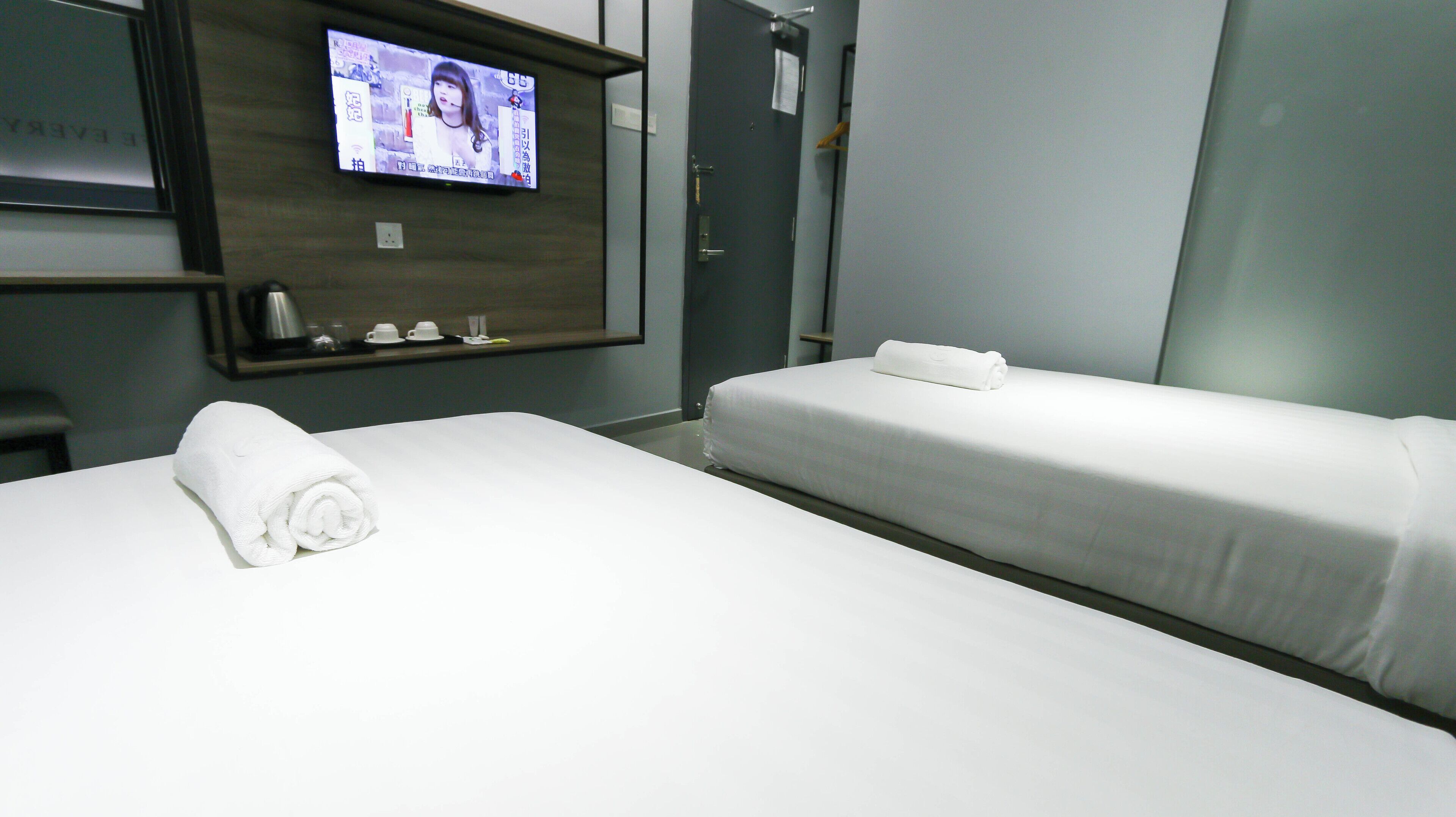 Une chambre d’hôtel avec deux lits, un téléviseur fixé au mur et une serviette sur le lit situé à gauche.