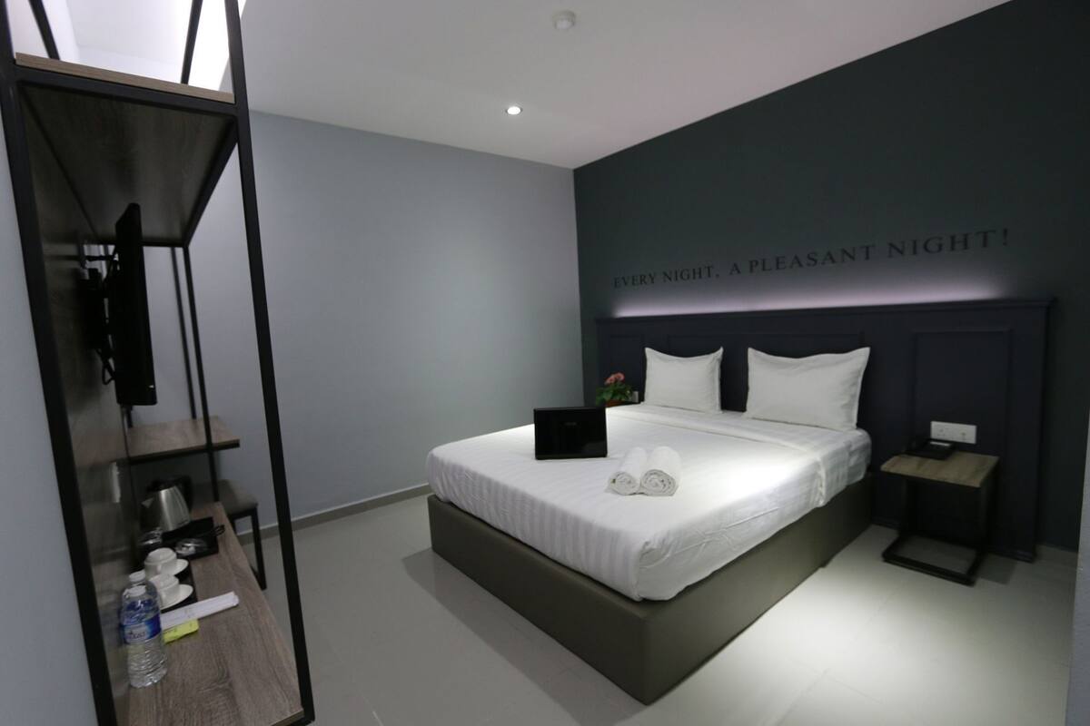 A modern hotel room with a large bed, bedside tables, a TV, and a wall with a message.