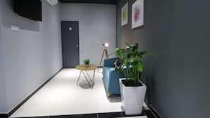 A modern hallway with a flat-screen TV, a potted plant, a blue sofa, and a small table.