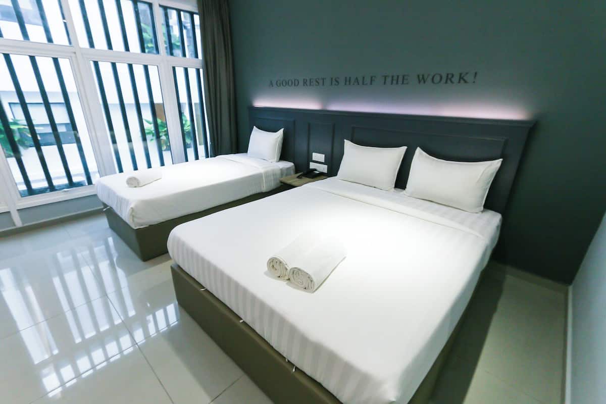 A hotel room with two beds, a large window with blinds, and a motivational quote on the wall.