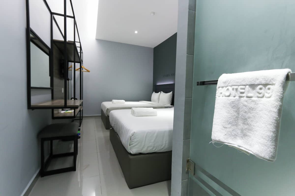 A modern hotel room with two beds, a bench, a mirror, and a towel hanging on the door.