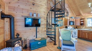 Een gezellig chaletinterieur met houten inrichting, een spiltrap, een televisie, een open haard en een keukenhoek.