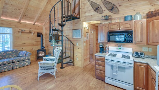 Een houten cabin interieur met een spiltrap, een keuken met fornuis en magnetron, een bank en een open haard.