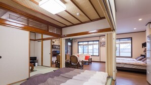 Une pièce de style japonais traditionnel, avec un sol recouvert de tatamis, un lit avec une couverture à rayures, un plafond en bois et une porte coulissante donnant sur une autre pièce.