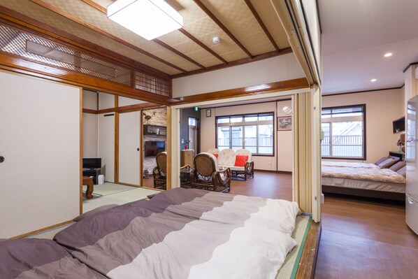 Une pièce de style japonais traditionnel, avec un sol recouvert de tatamis, un lit avec une couverture à rayures, un plafond en bois et une porte coulissante donnant sur une autre pièce.