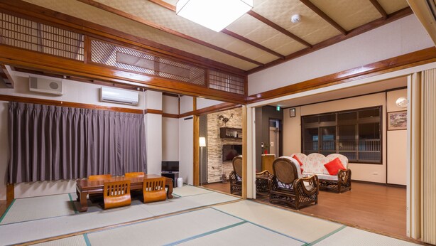 Une pièce de style japonais traditionnel, avec un sol recouvert de tatamis, une table en tatami entourée de chaises, un canapé avec des coussins et un plafond en bois agrémenté d’un paravent shoji.