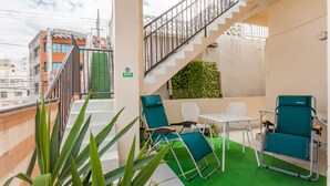 Une terrasse sur le toit, équipée de deux chaises longues, d’une petite table et d’un escalier menant à un niveau supérieur.