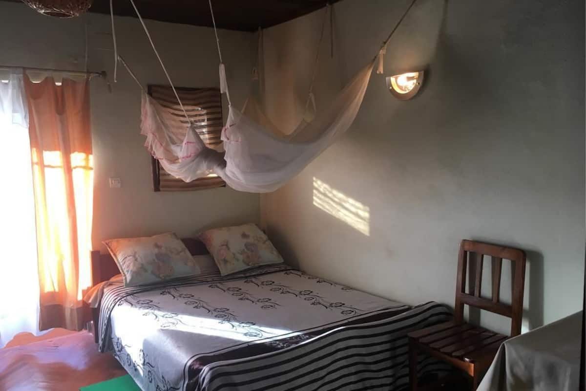 Un dormitorio con cama, una silla, una hamaca colgante y una mesa.